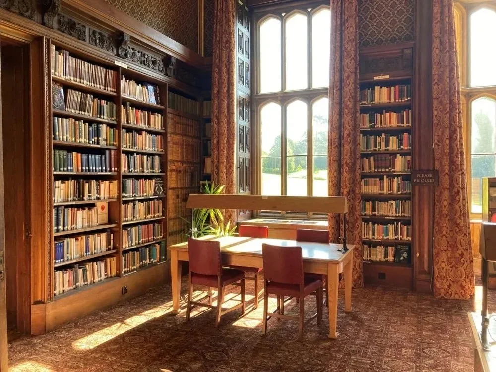 The wood-panelled library at Wroxton Abbey, with reading tables beneath a tall mullioned window